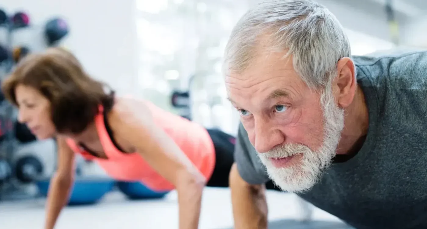 Two adults exercising with push-ups in a gym, representing wellness and peptide therapy.
